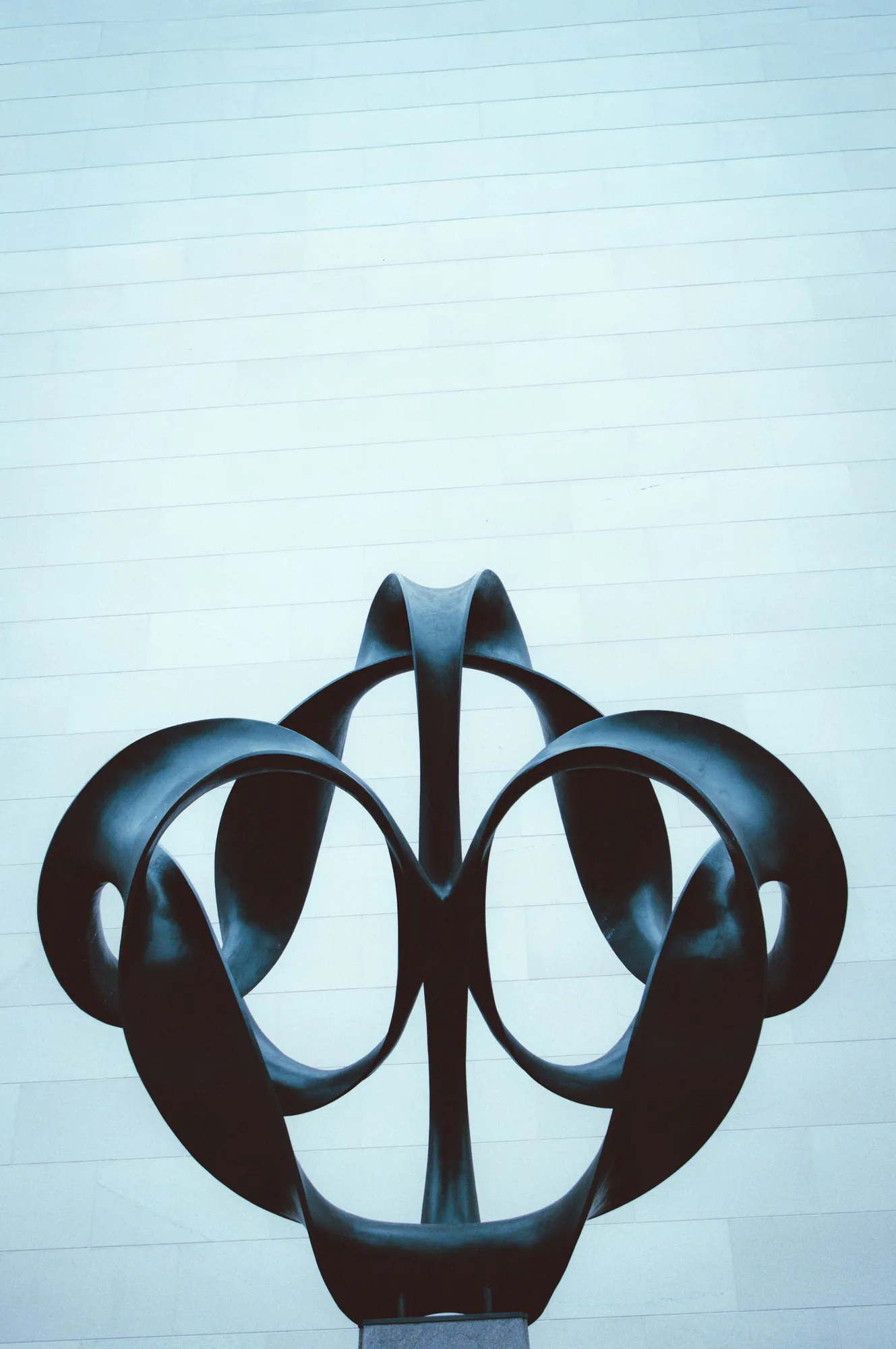 Abstract black sculpture set against a minimal pale wall.
