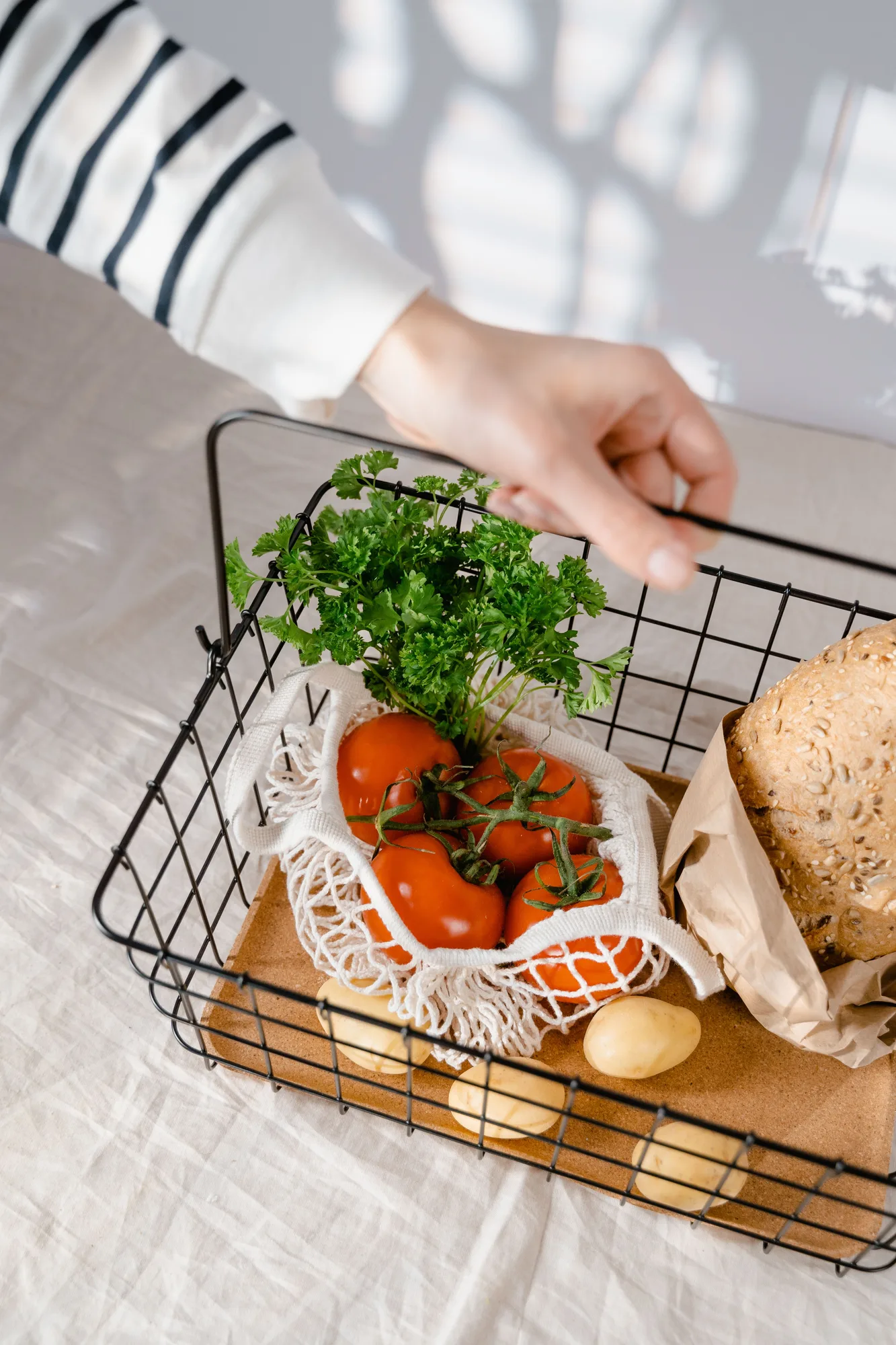 A hand reaching into a basket of tomatoes, herbs and bread