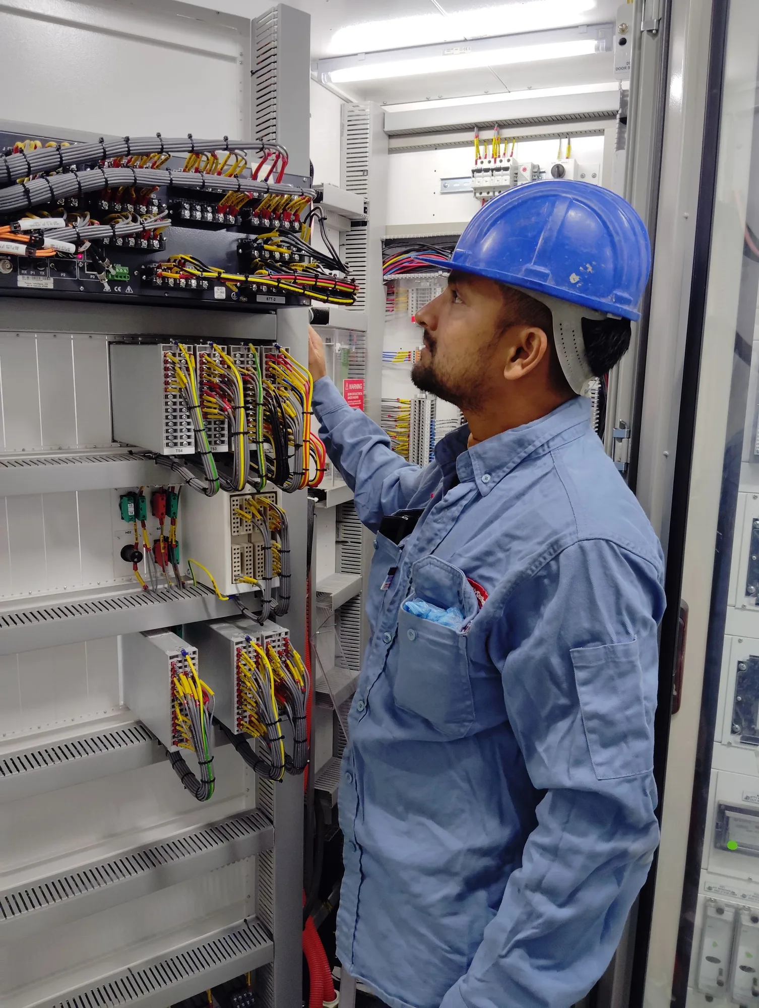 Worker in a blue helmet beside an industrial control panel