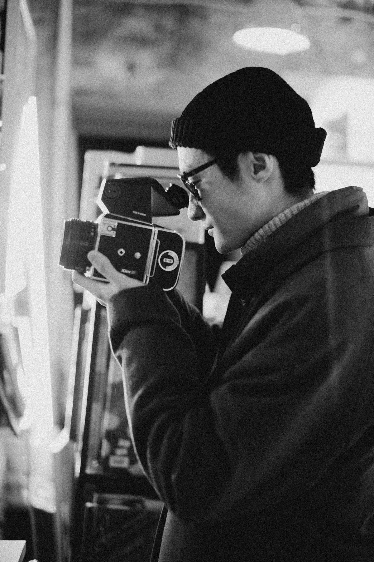 A photographer working with a film camera beside a window.