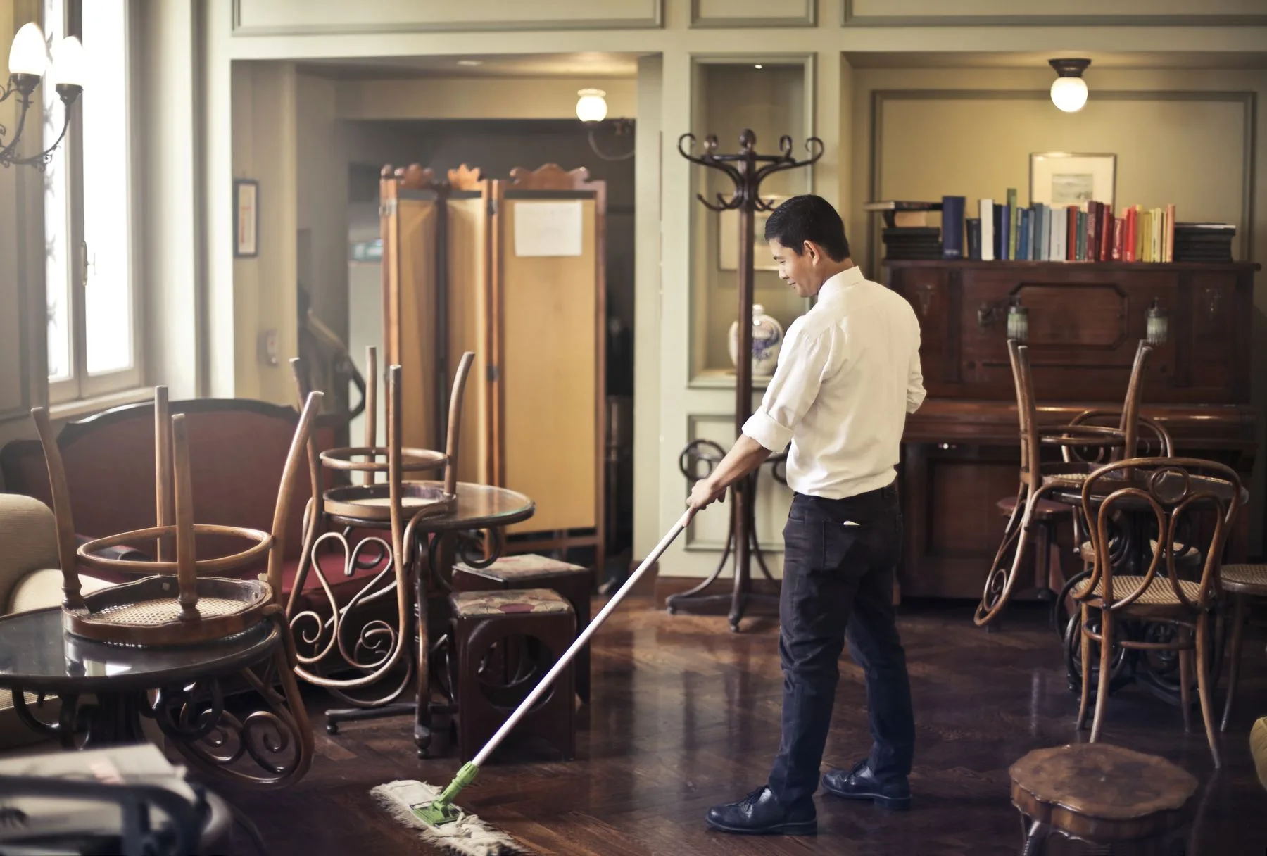 A person mopping a cafe floor with chairs stacked nearby