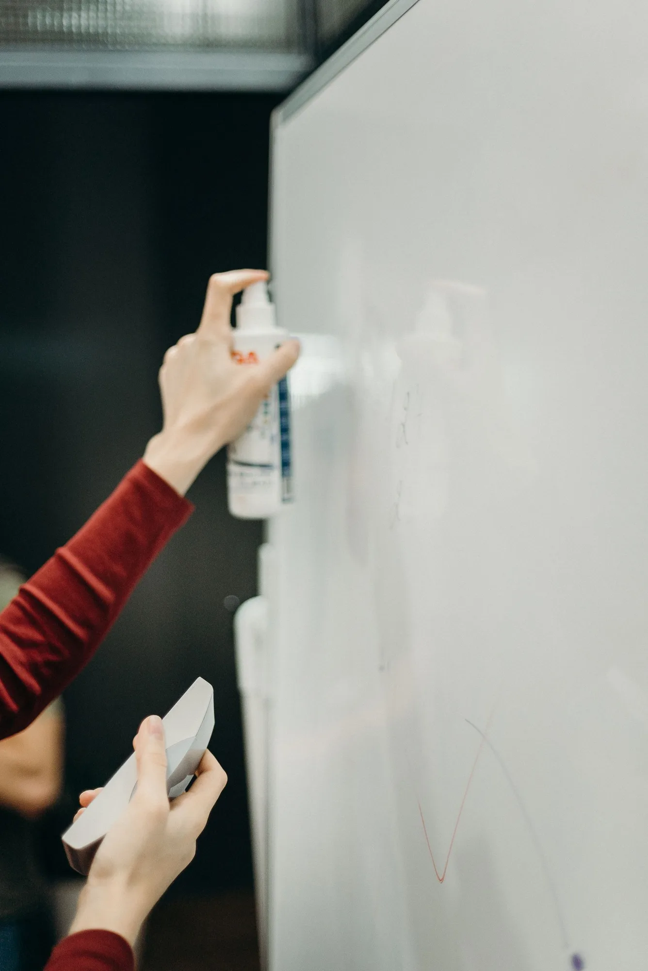 Hands using spray and a cloth on a whiteboard