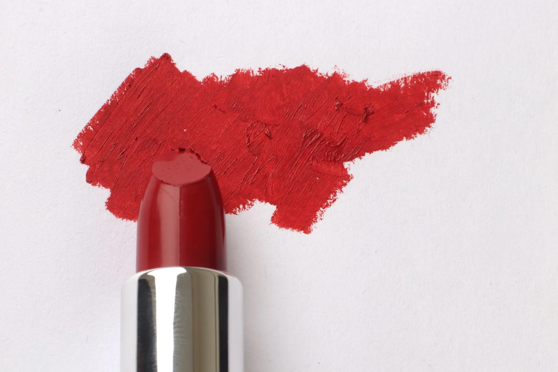 A red lipstick and a bold pigment stroke on white paper.