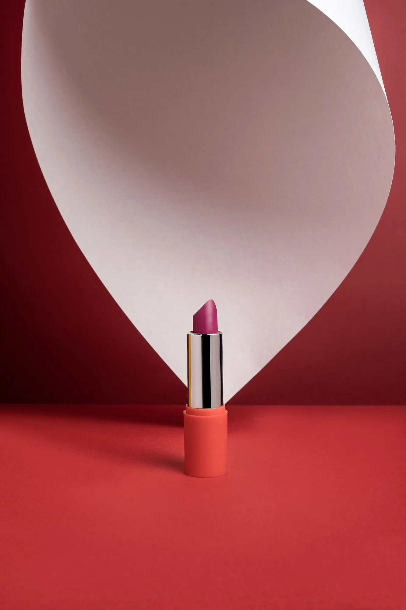 Berry lipstick standing among sculptural red paper folds.
