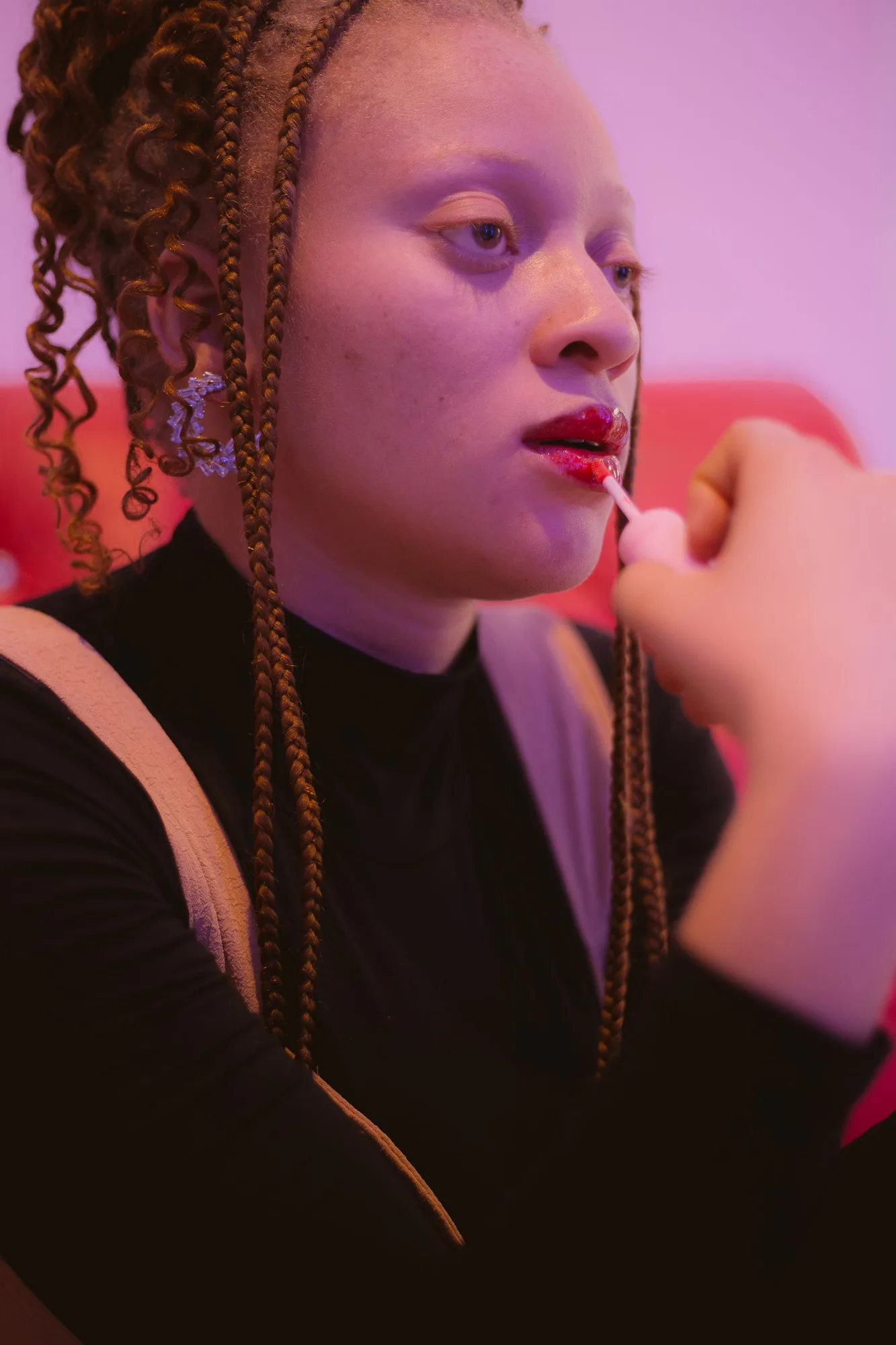 A woman applying lip color against a vivid pink background.