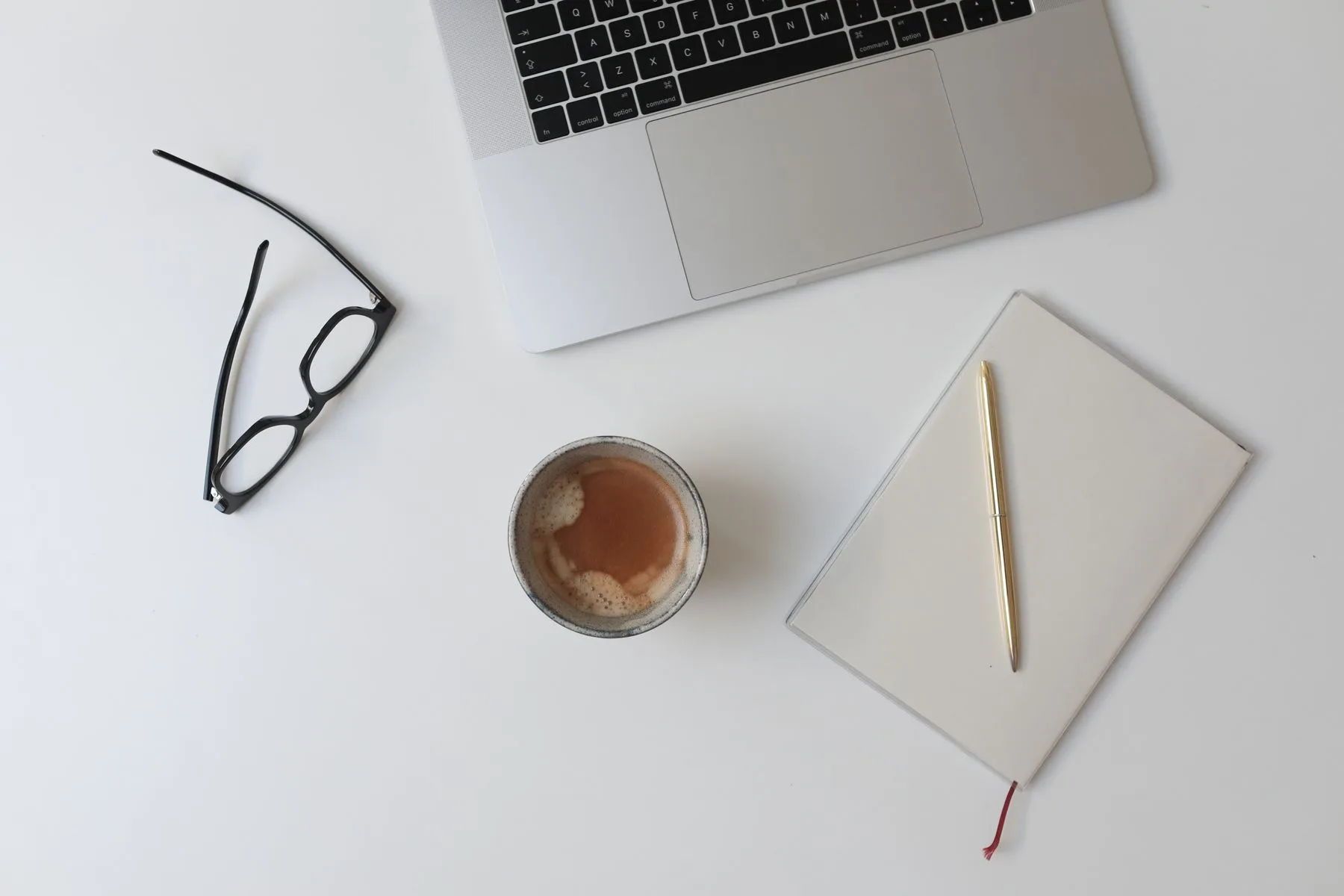 An overhead arrangement of a laptop, notepad, coffee and glasses.