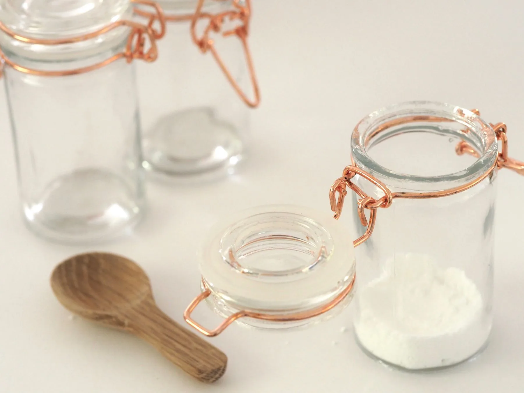 Clear glass storage jars with copper closures and a wooden spoon