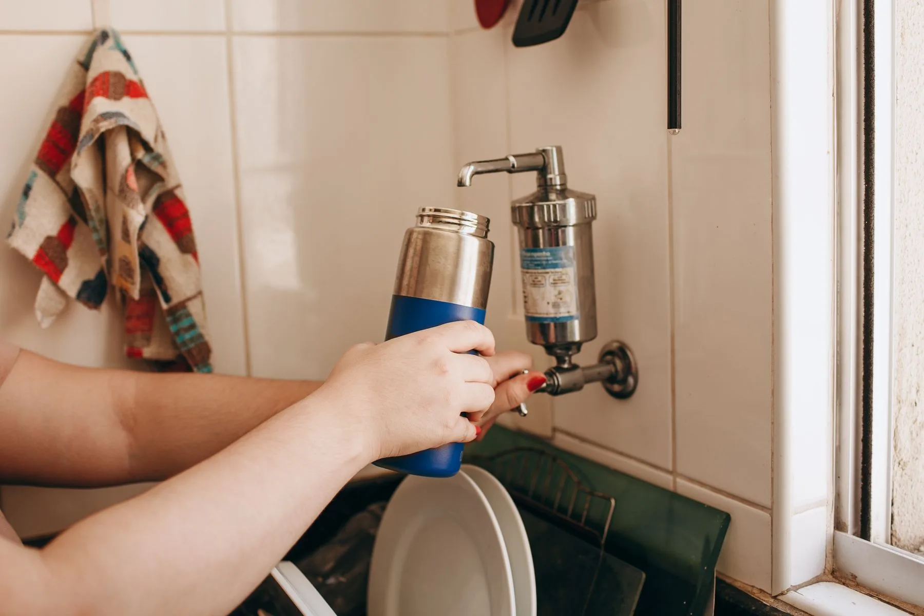 Hands filling a reusable water bottle at a kitchen sink