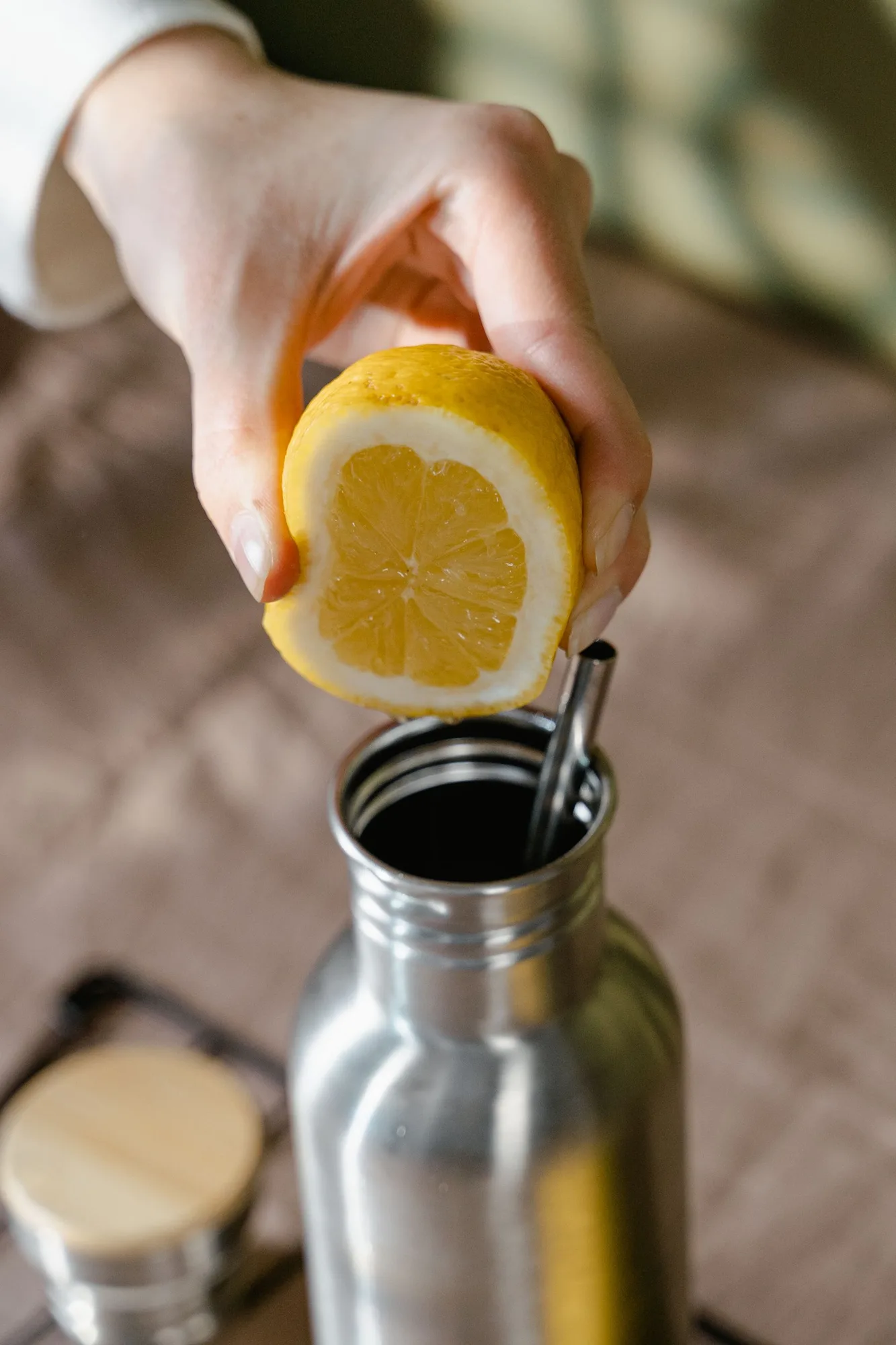 Hand squeezing a lemon into a stainless steel bottle