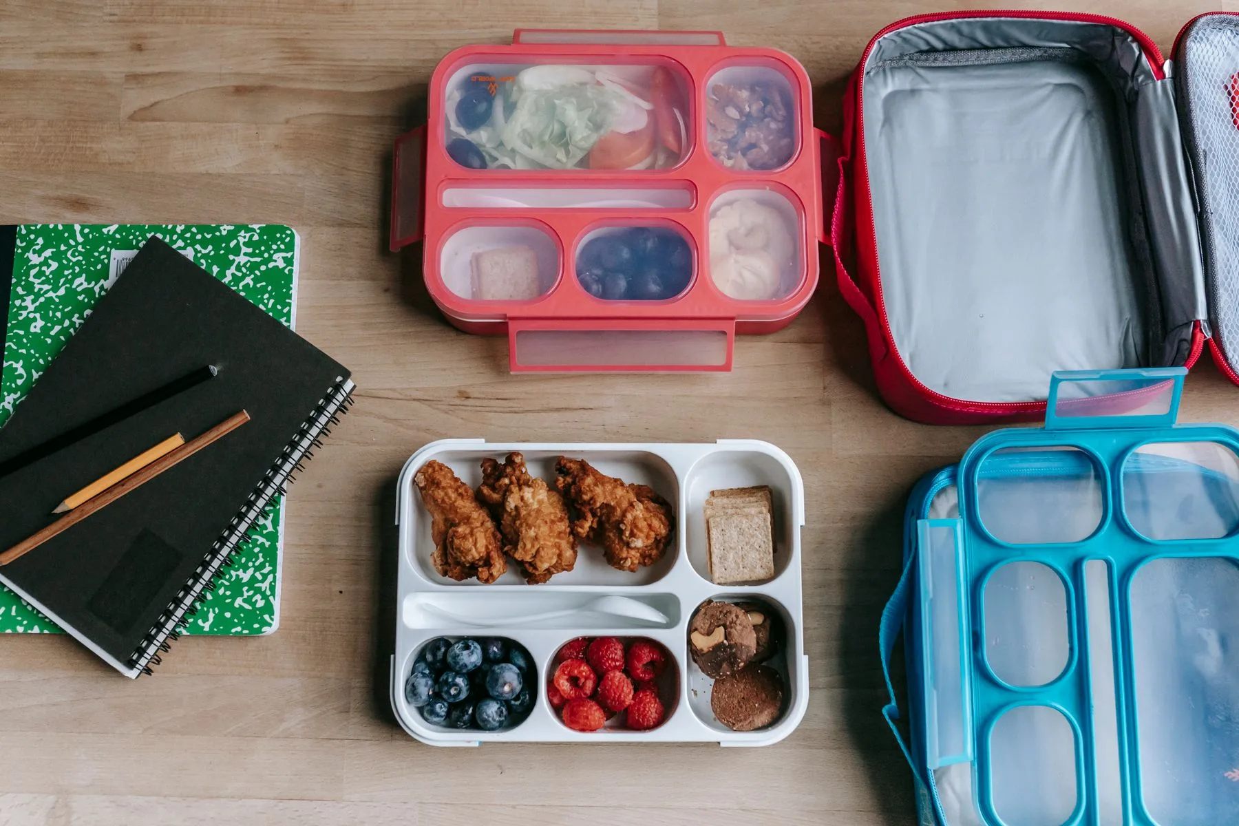 Lunchboxes with food beside notebooks on a desk