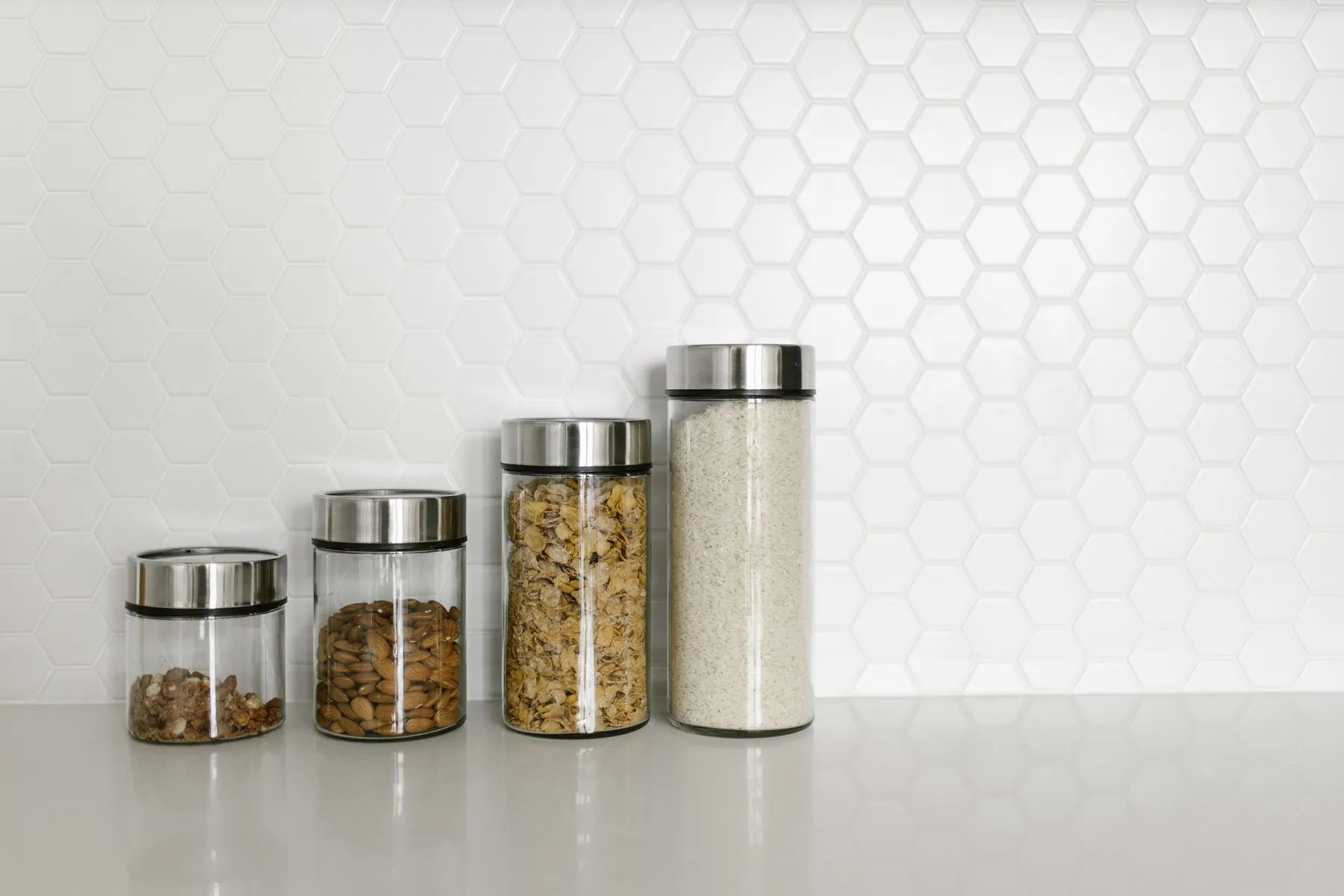 Glass jars filled with dry goods against white kitchen tiles