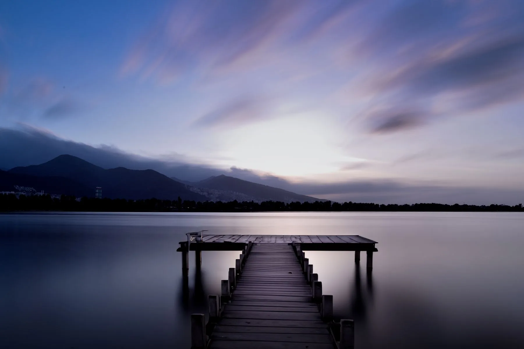 A wooden pier extending into a calm lake beneath distant mountains.