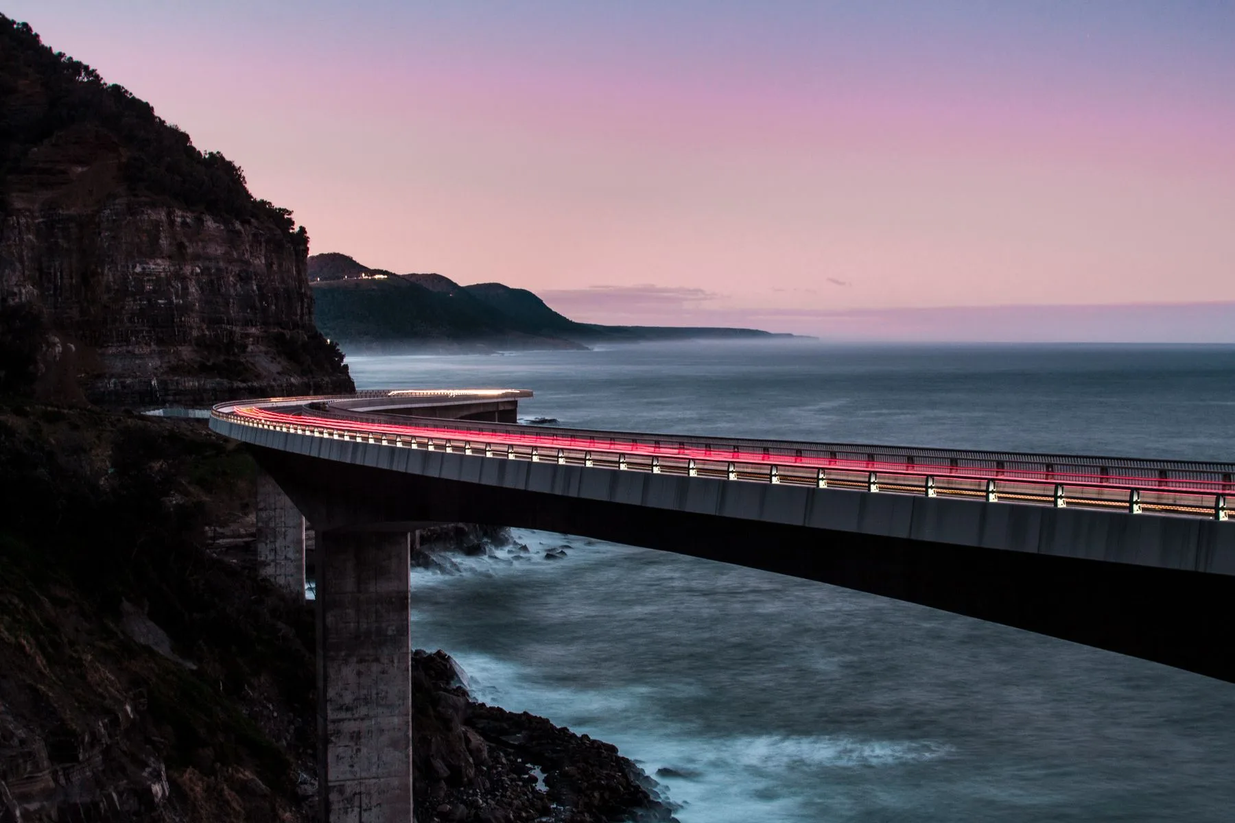 A coastal bridge curving beside the ocean in the evening light.