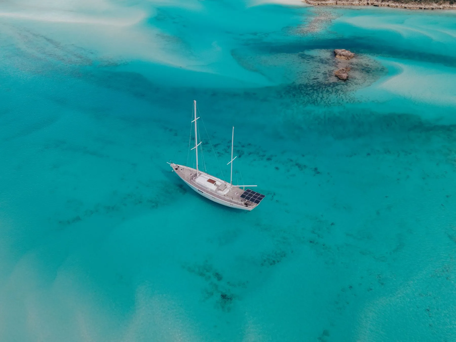 A sailboat viewed from above on clear blue ocean water.