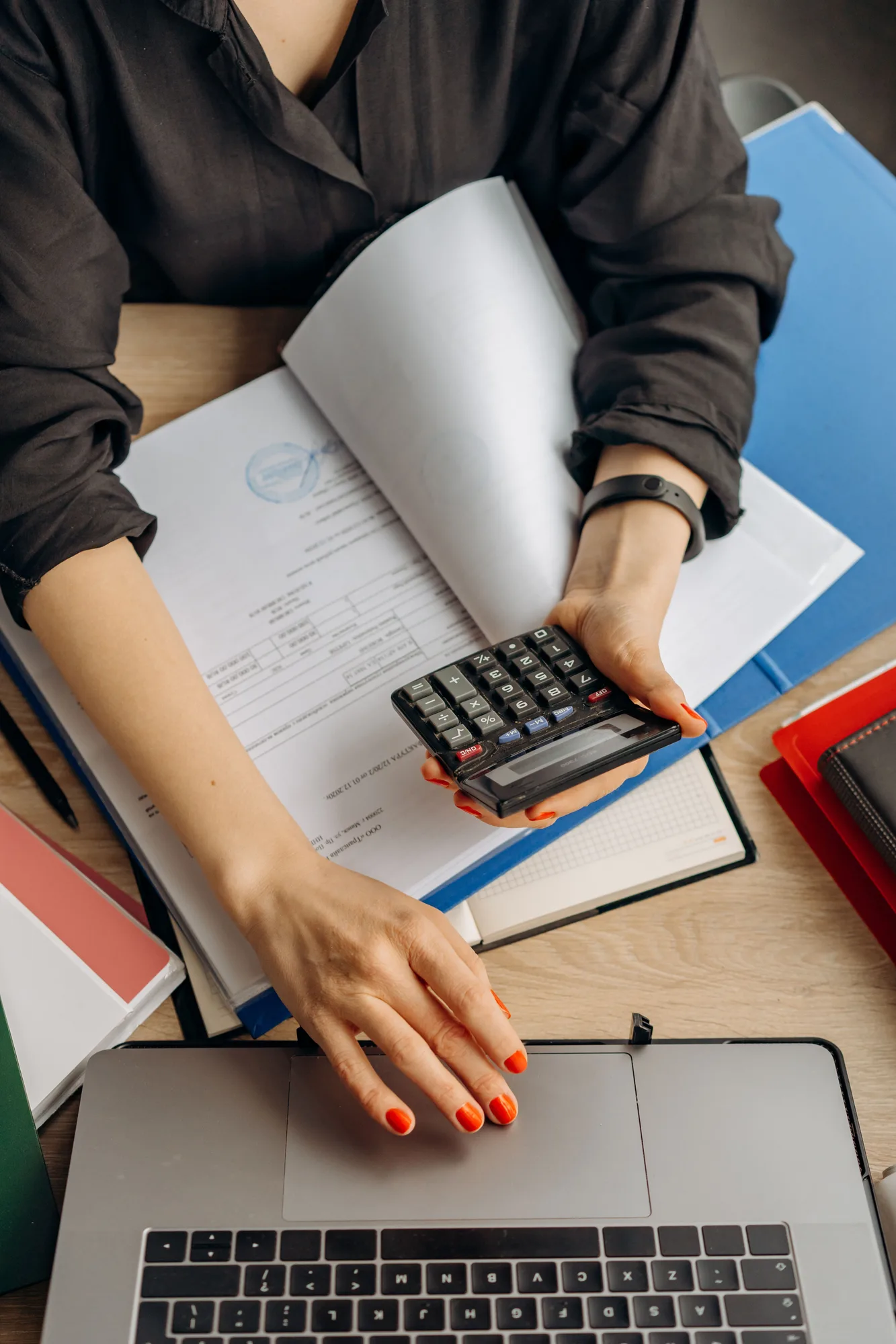 A person holding a calculator beside paperwork and a laptop