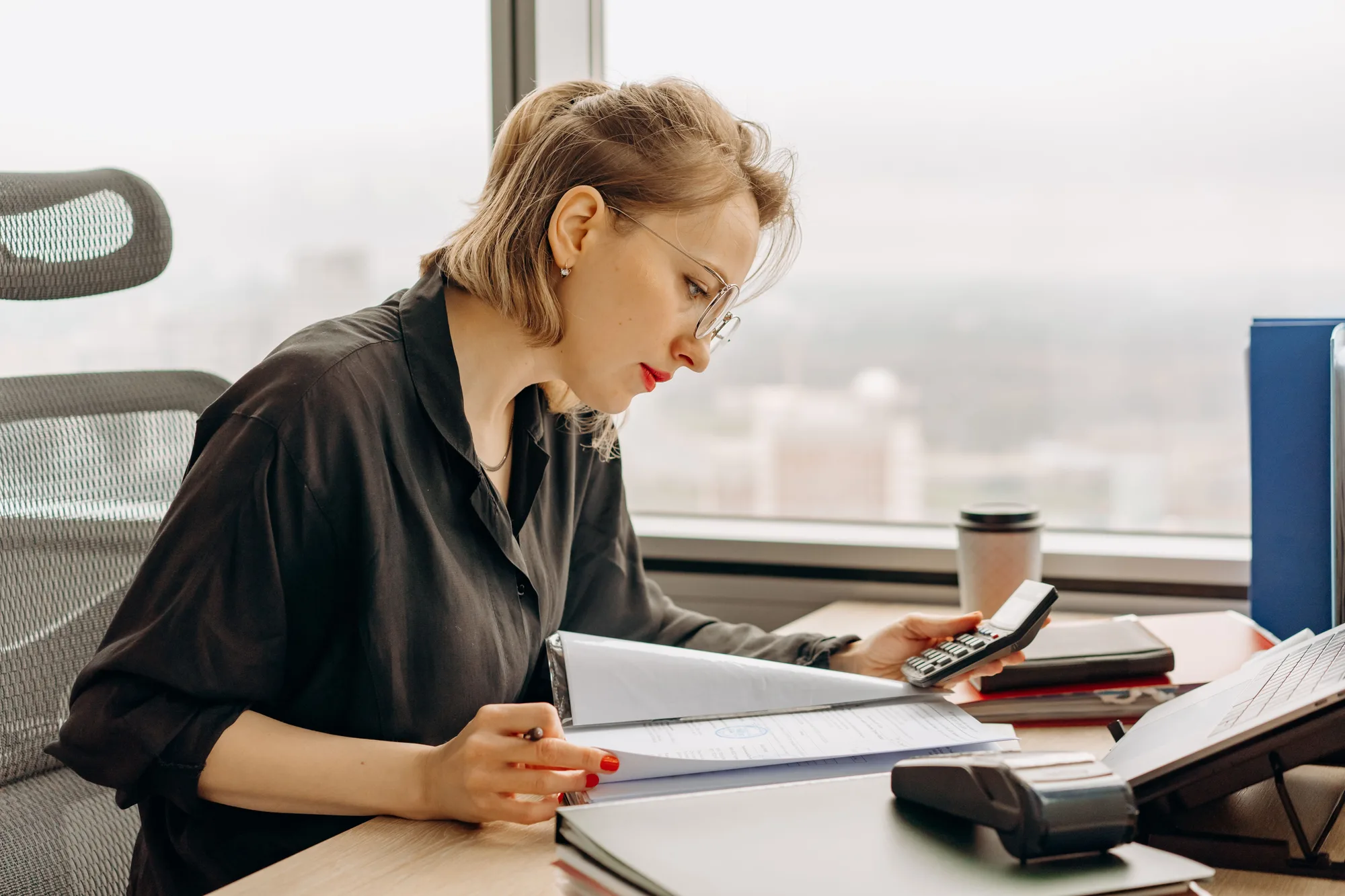 A woman with glasses working at a desk with documents and a calculator