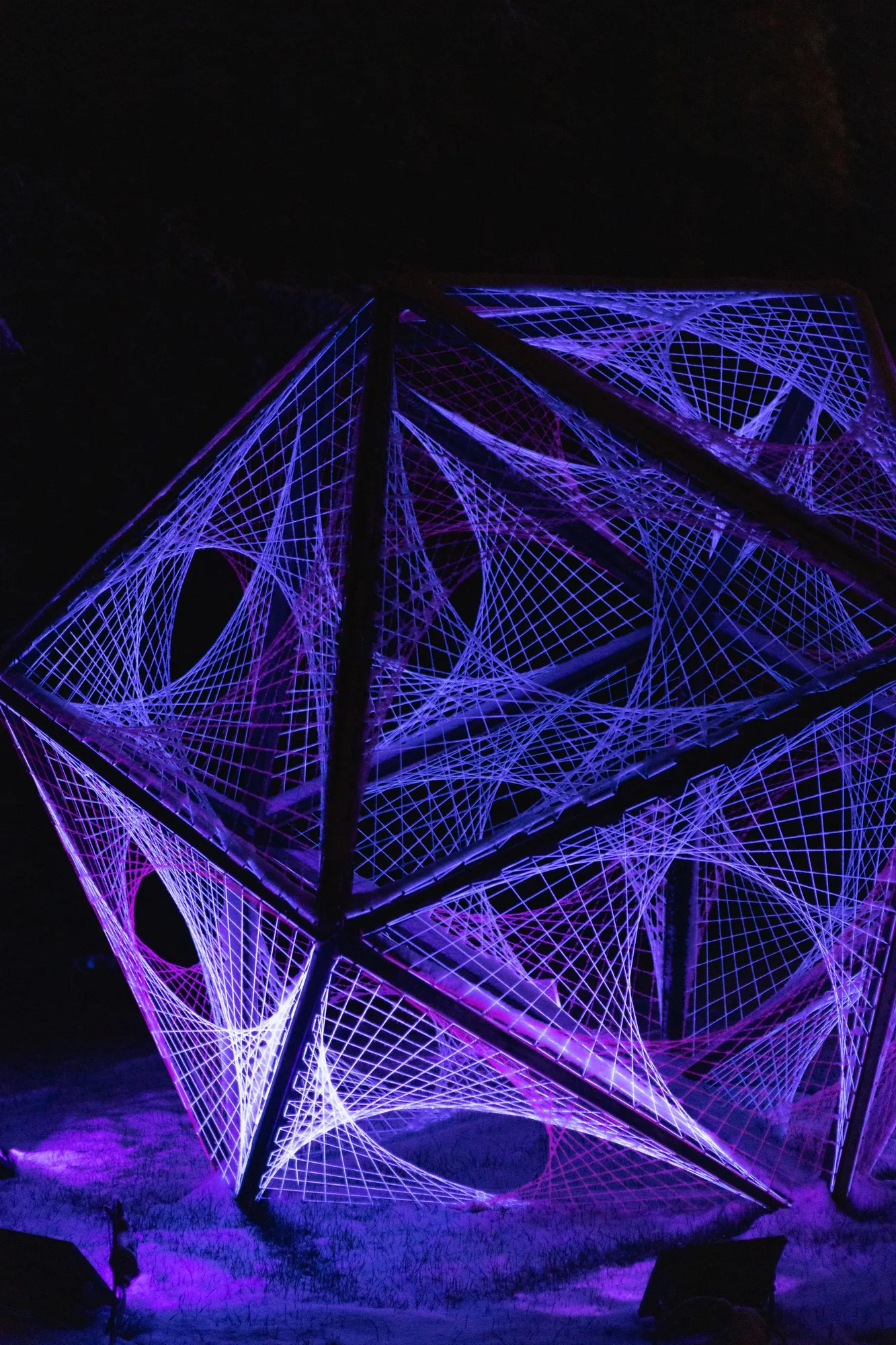 Purple light illuminating a geometric string installation against darkness.
