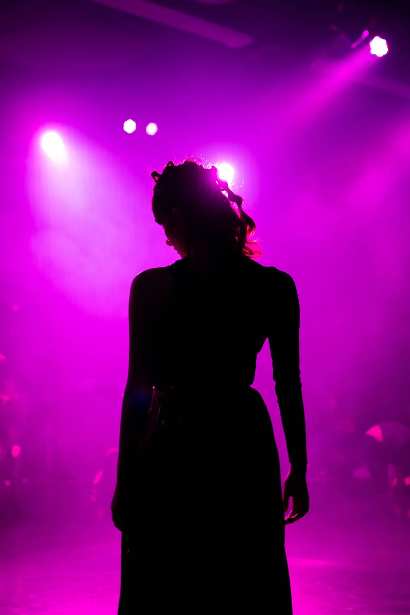 A silhouetted performer beneath vivid purple stage lighting.