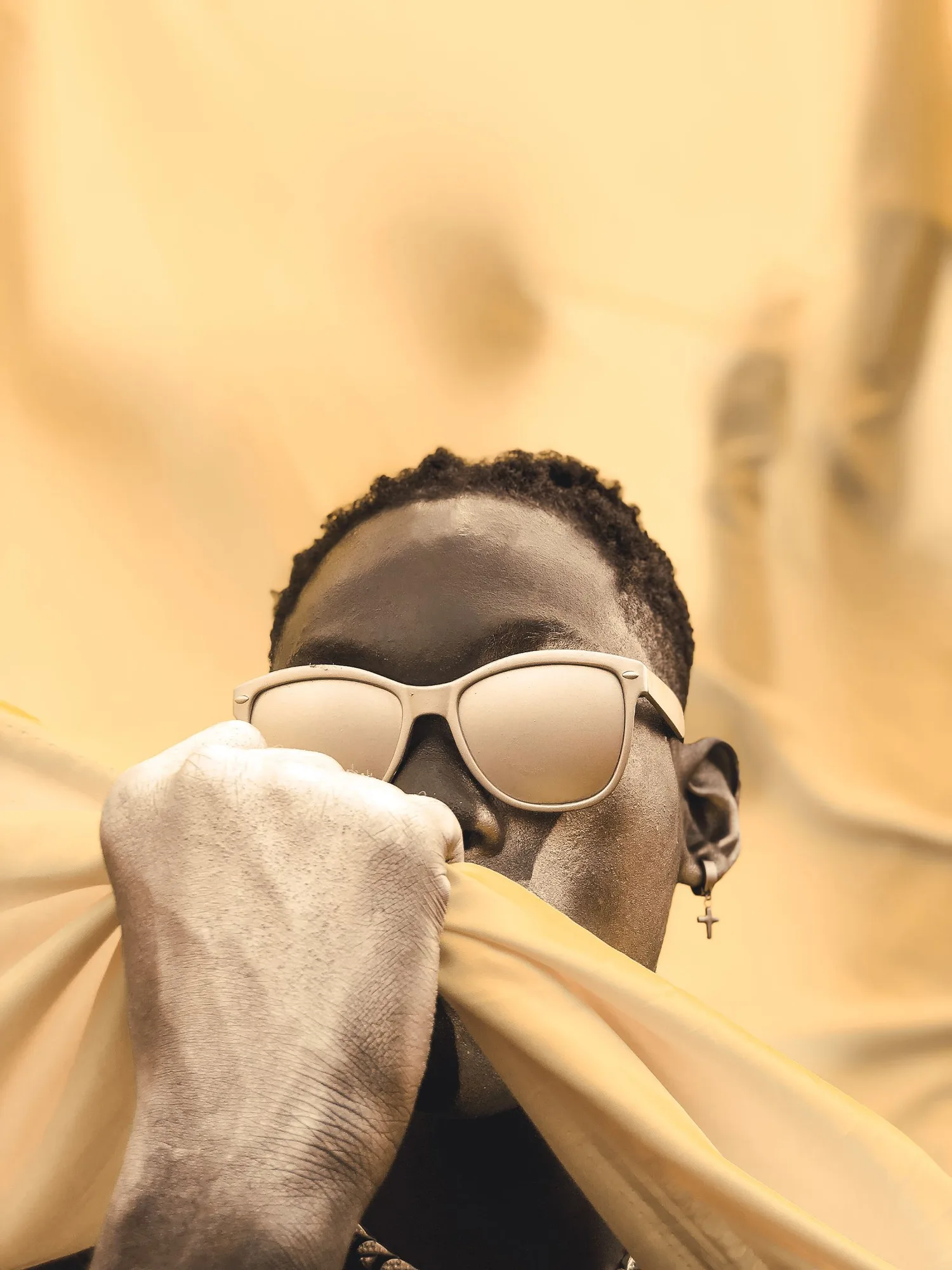 A man wearing sunglasses against a bright yellow studio background.