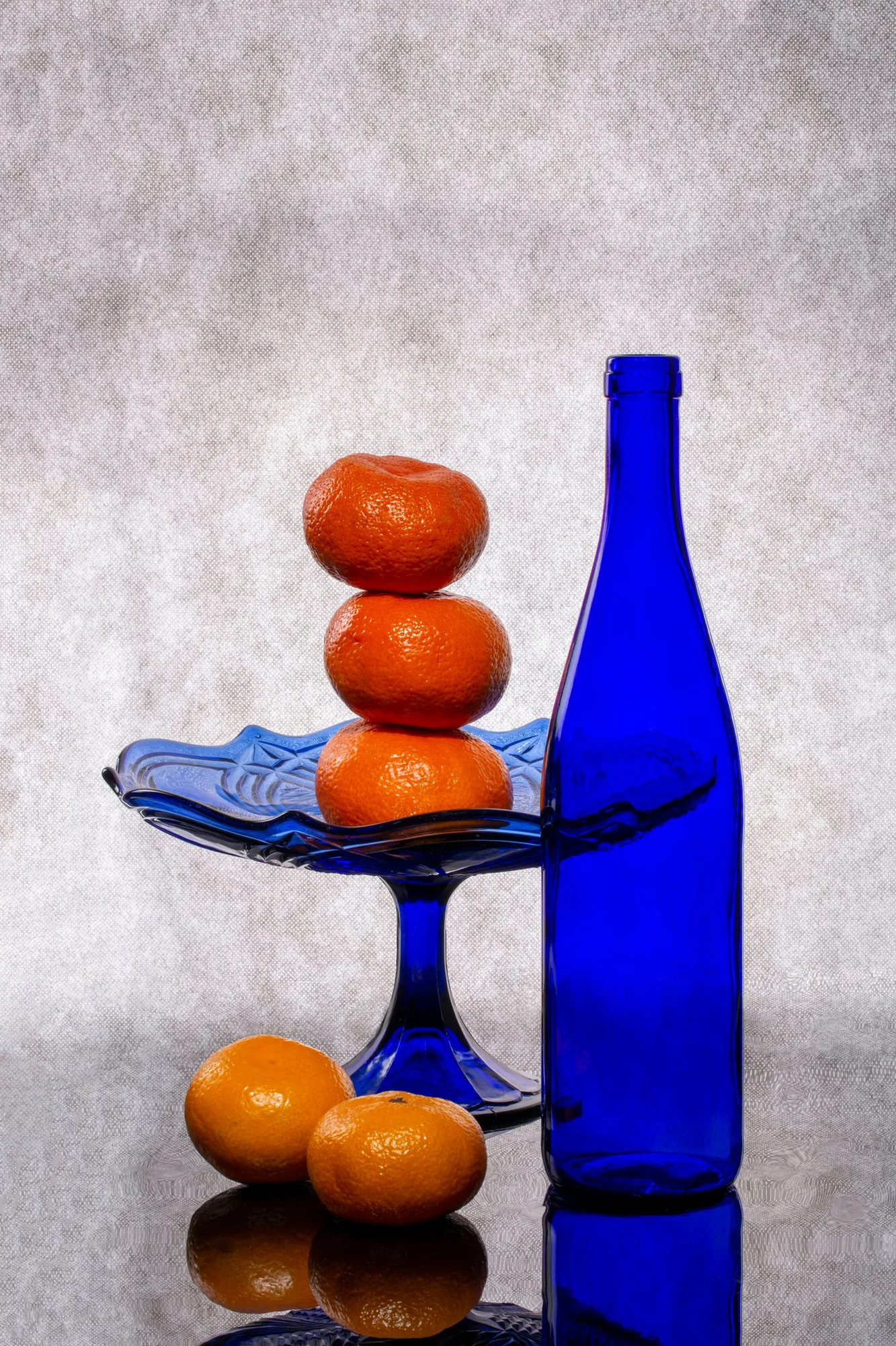 Oranges and a cobalt blue glass bottle arranged in a reflective still life.