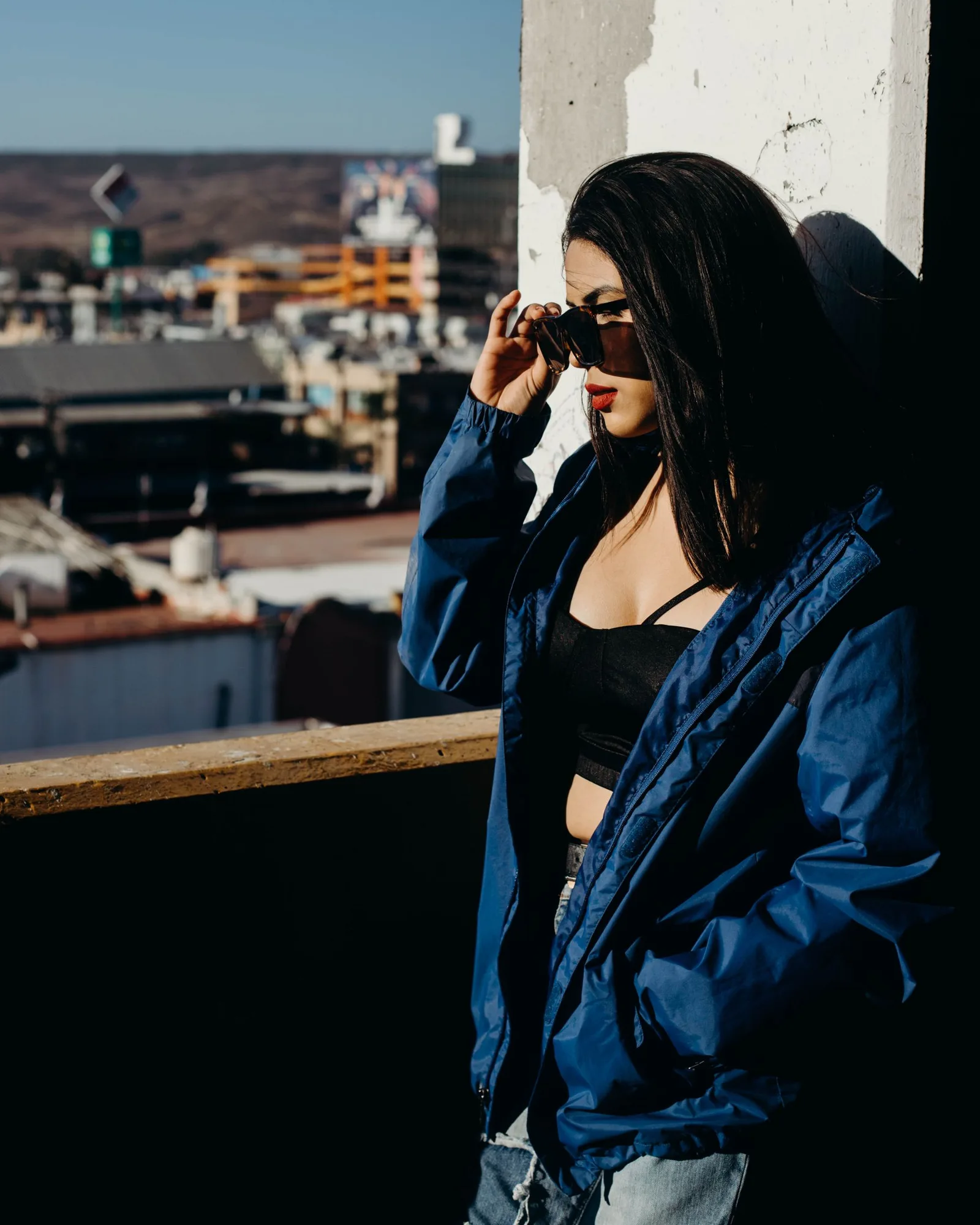 Woman in a blue jacket and sunglasses against a city skyline