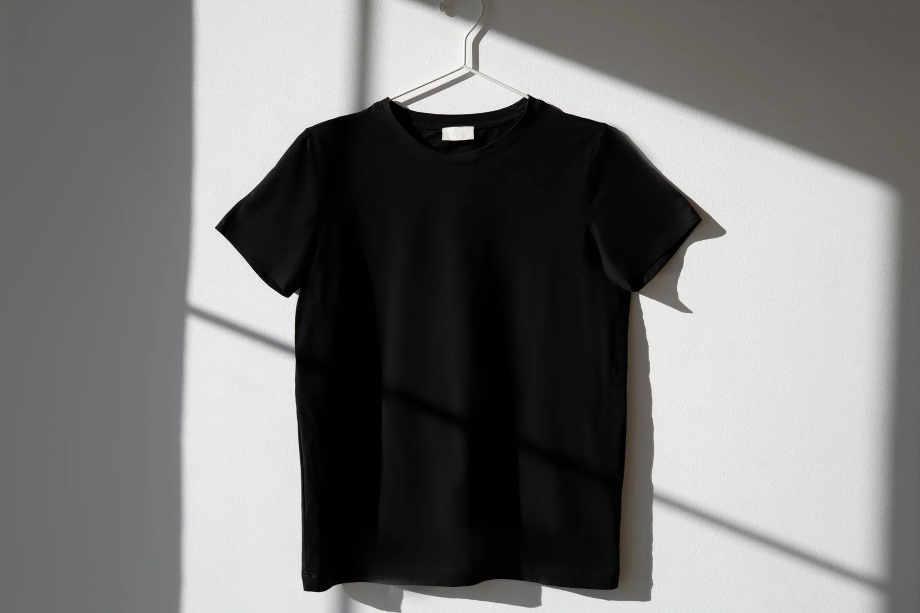 Plain black T-shirt on a hanger against a white wall