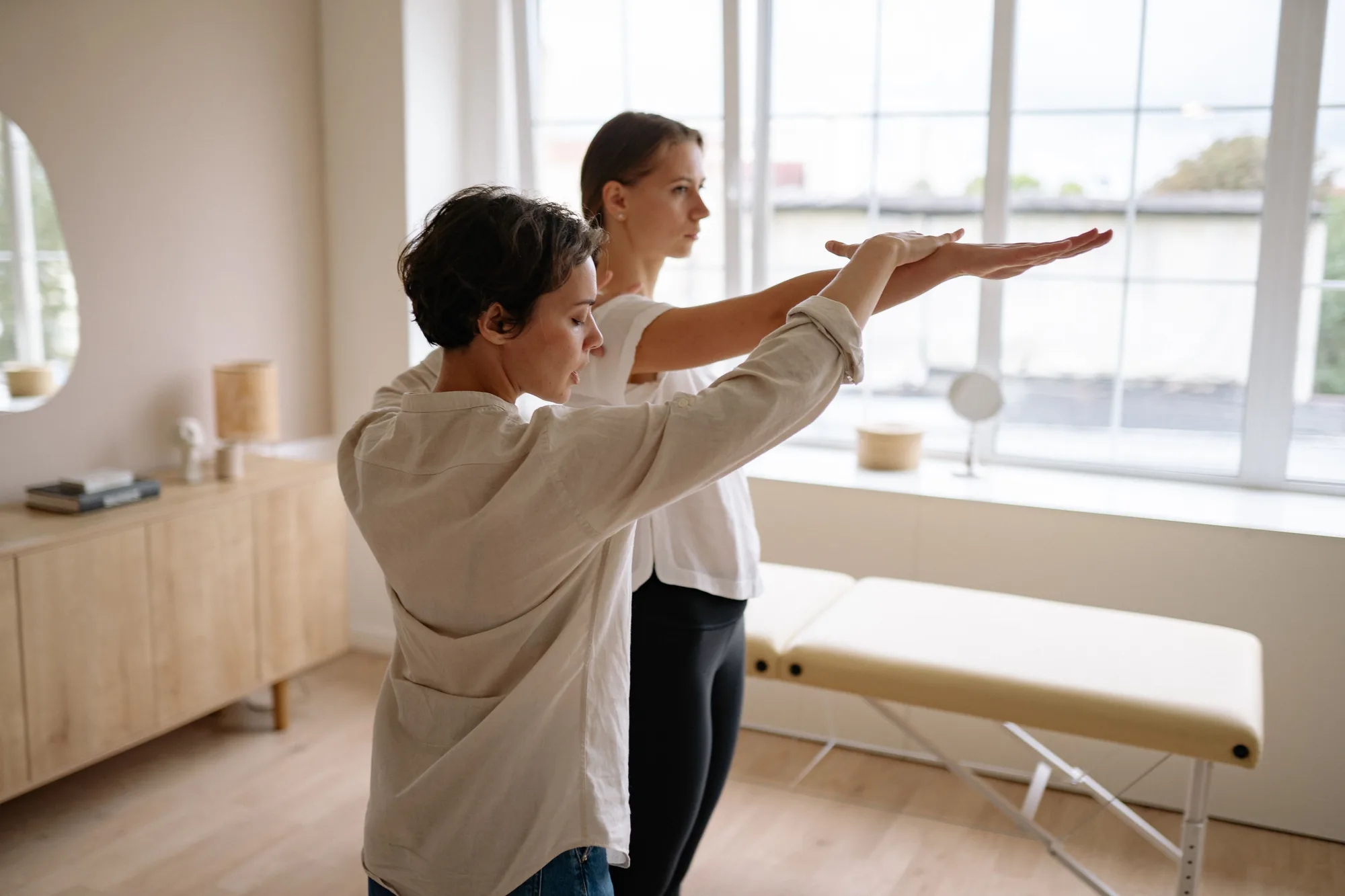 A therapist assisting a woman with an exercise in a bright treatment room