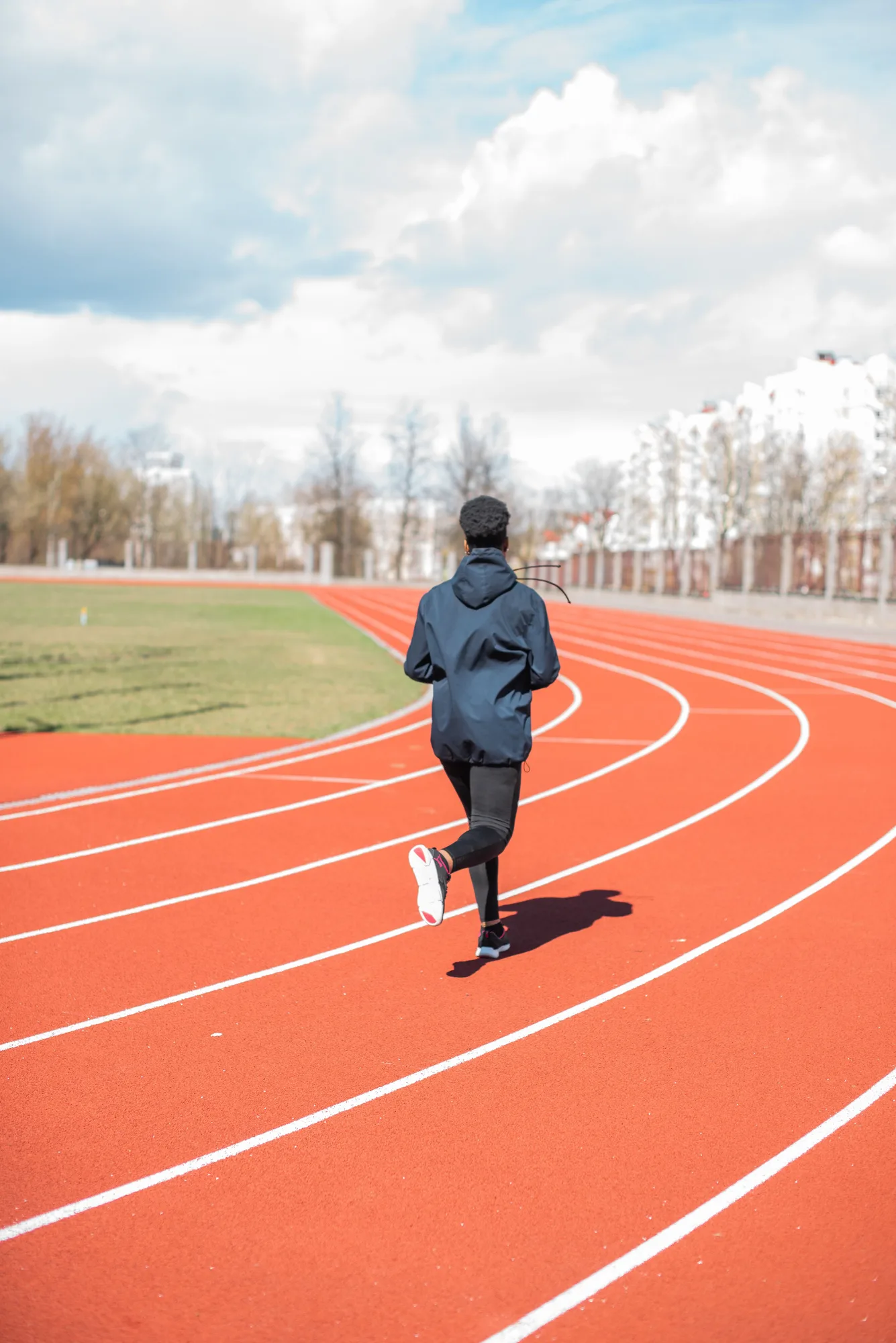 A runner in a blue jacket moving along a red outdoor track