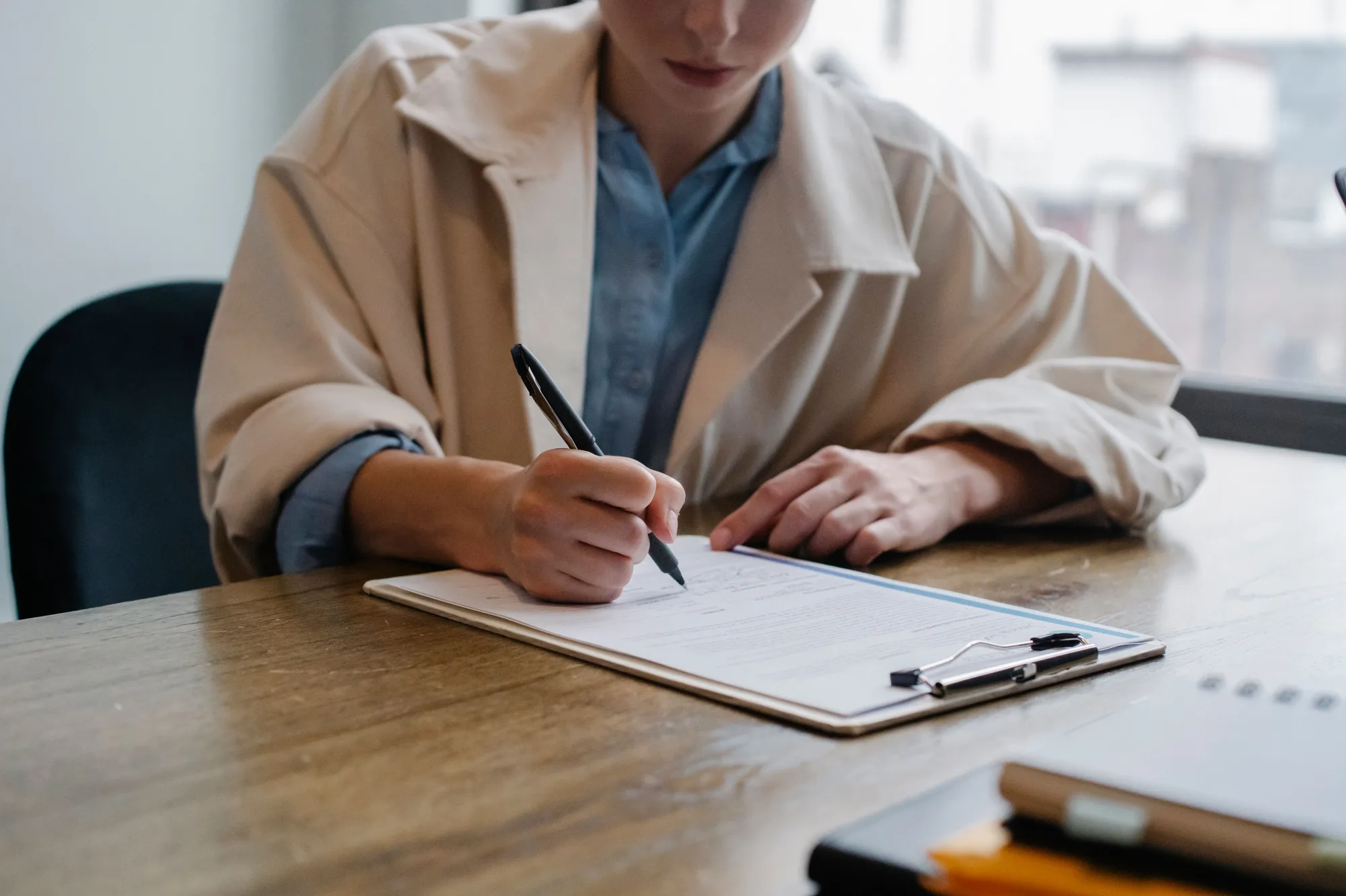 A woman writing on a clipboard beside a laptop at a desk