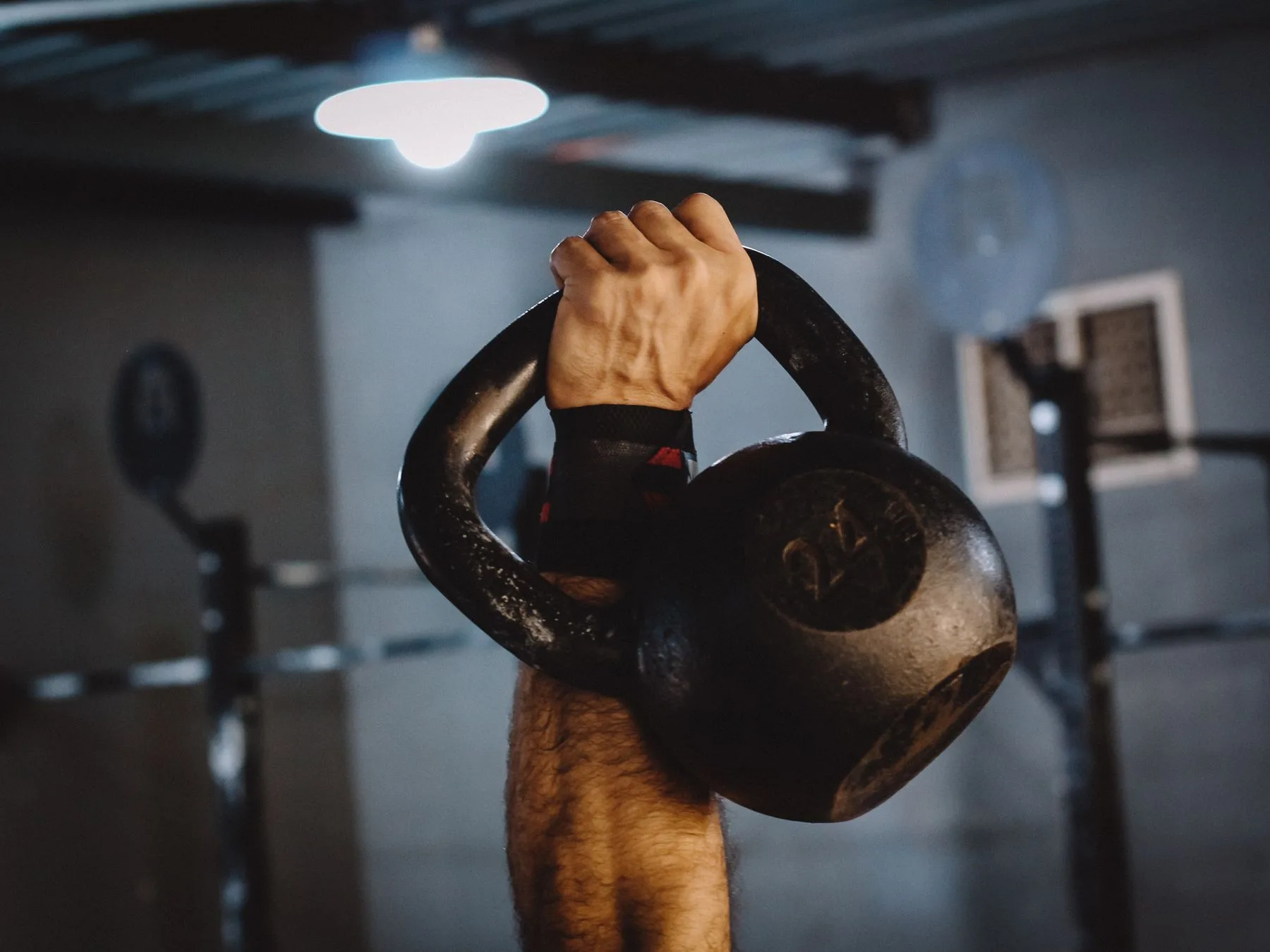 A close view of a hand holding the handle of a black kettlebell.