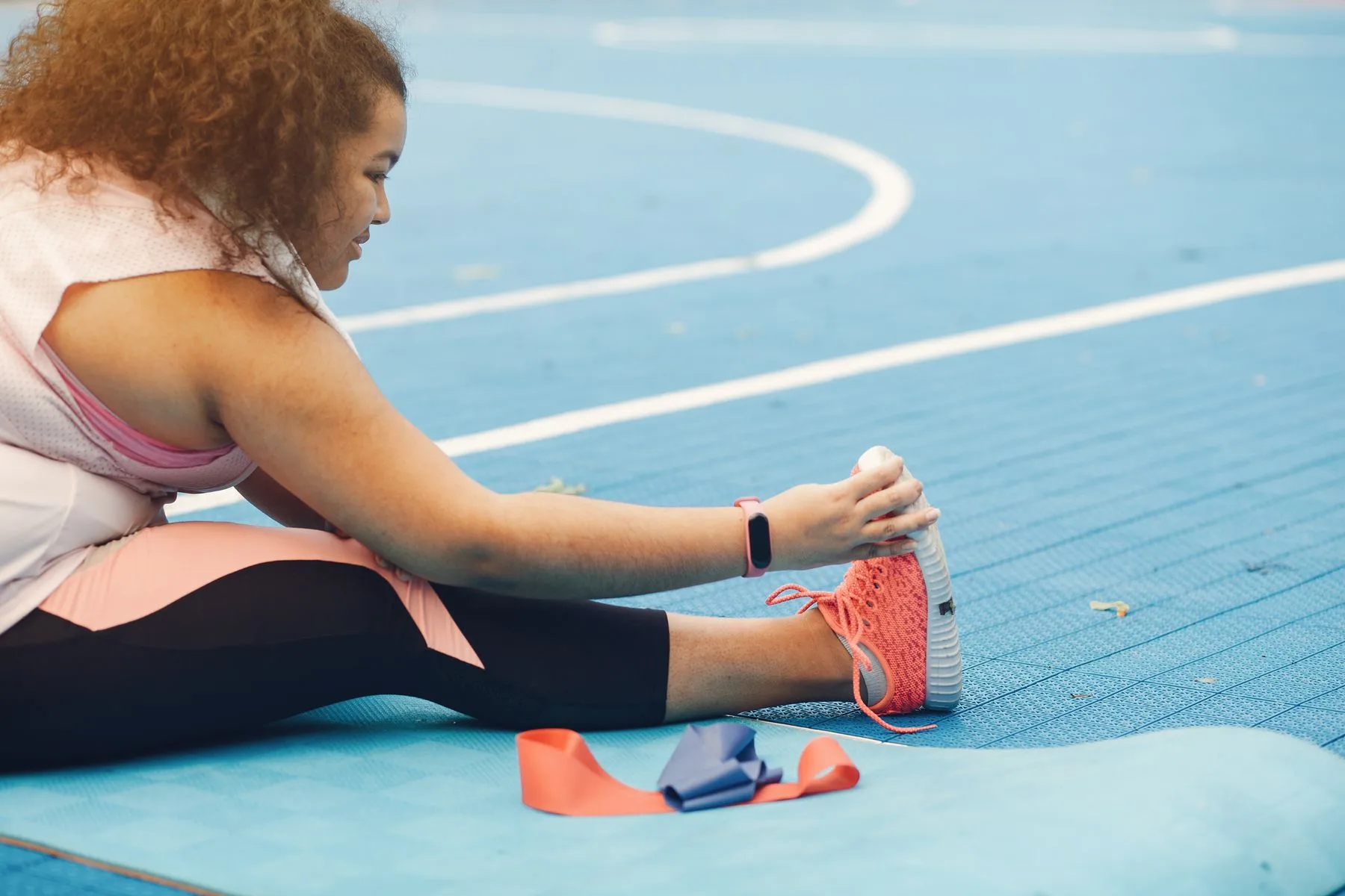 A woman stretching on a blue outdoor court.