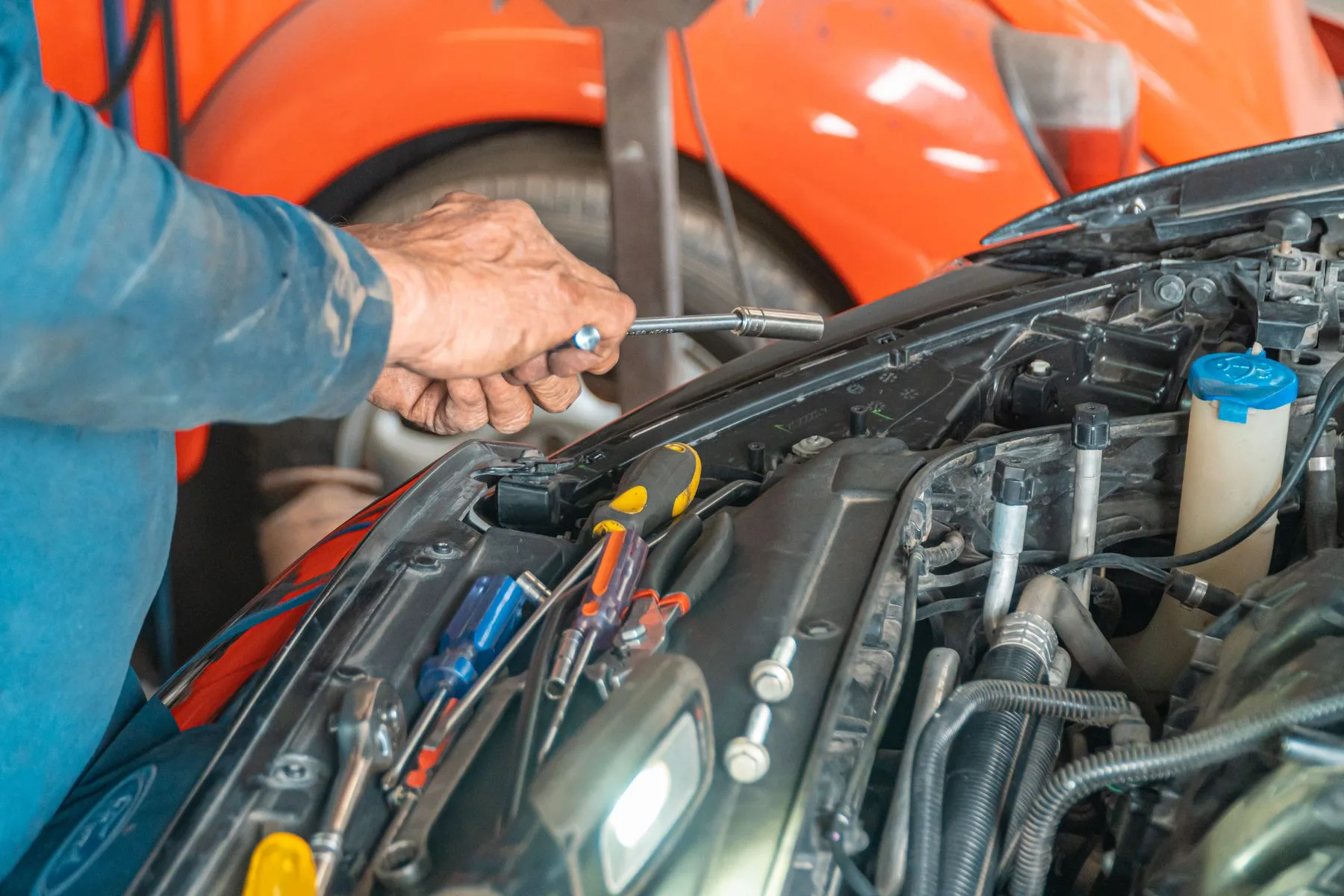 Hands using a tool beside an open car engine